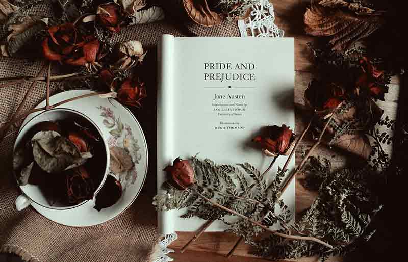 Jane Austen Pride and Prejudice book open on table with roses and cup of tea.